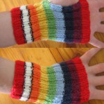 A pair of short ribbed rainbow handwarmers, with 2cm stripes in the following colours, from cuff to knuckles: red, white with black border, orange, yellow, green, blue, indigo, violet, red.