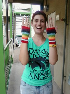 A person wearing a pair of rainbow knitted handwarmers, and looking quite chuffed about it, too.