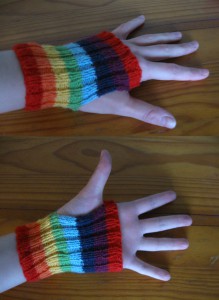 Small rainbow striped ribbed handwarmers, ie: a tube with a thumb hole. They reach from just below the wrist-bone to just on the first finger knuckles. The stripes are bright, as follows, from cuff to knuckle: red, orange, yellow, green, blue, indigo, violet, red.